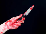 Bloody hand holding a bloody knife on a black background, Halloween concept